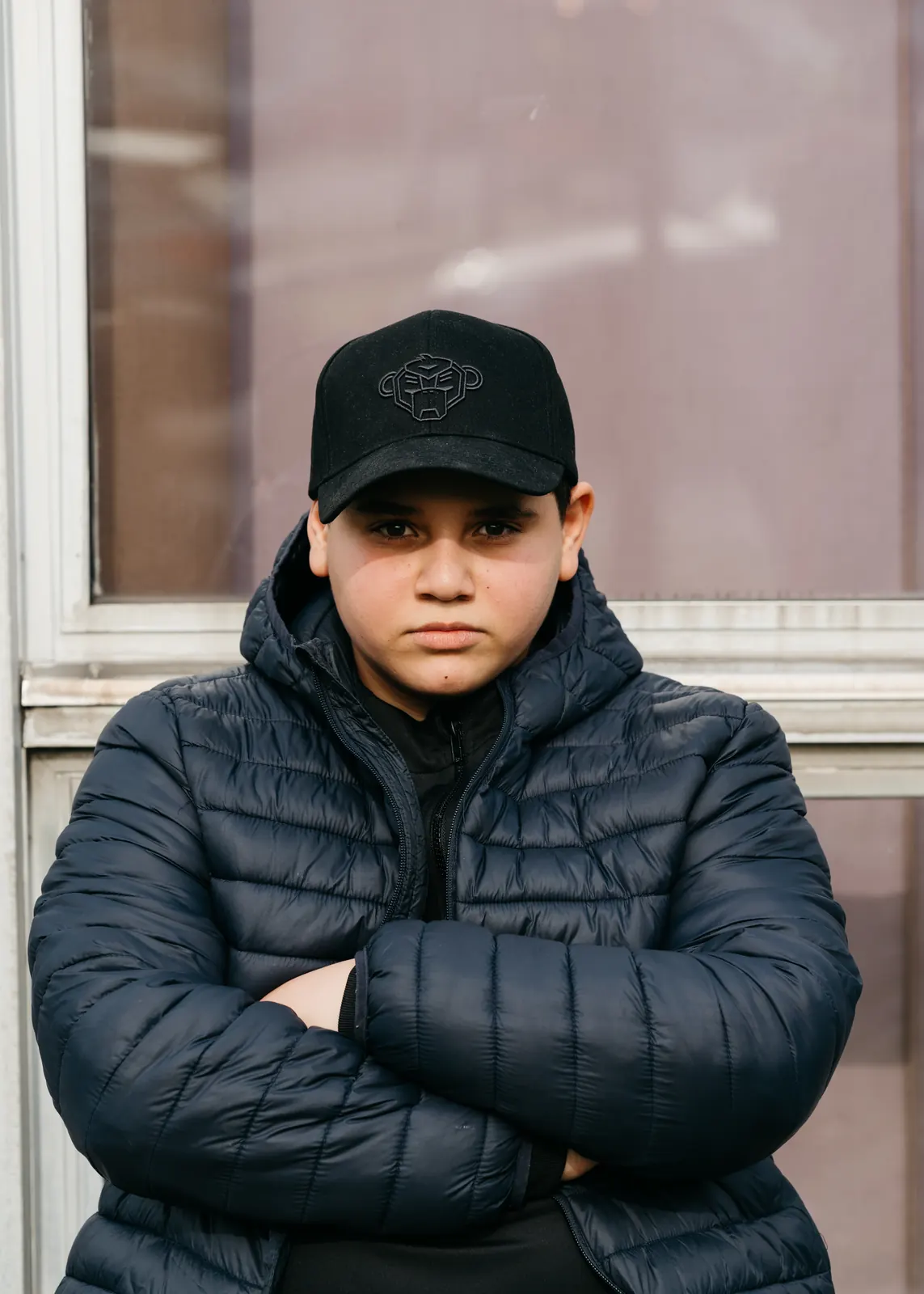Portret van een jongen met pet en donsjas, armen gekruist