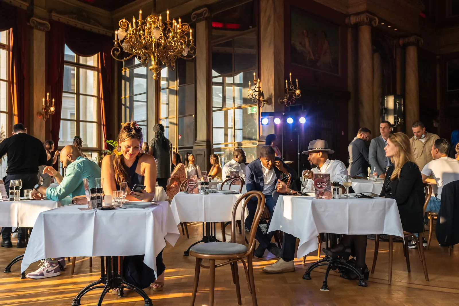 Gasten aan witgedekte tafels in een zonovergoten feestzaal met kroonluchter, tijdens een Jumping Judy-diner