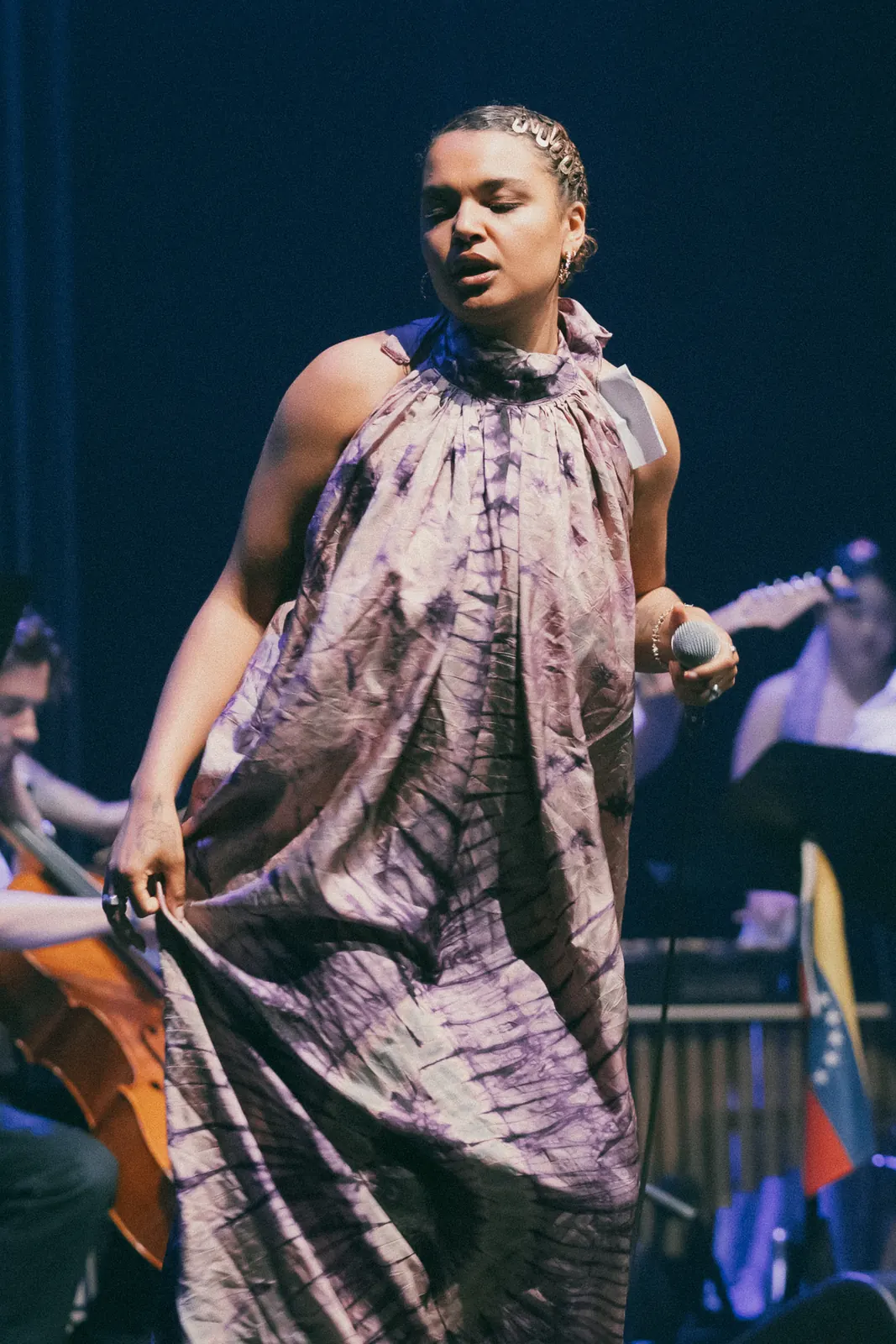 Zangeres in een paarse jurk zingt op het podium, met cello en orkest achter haar